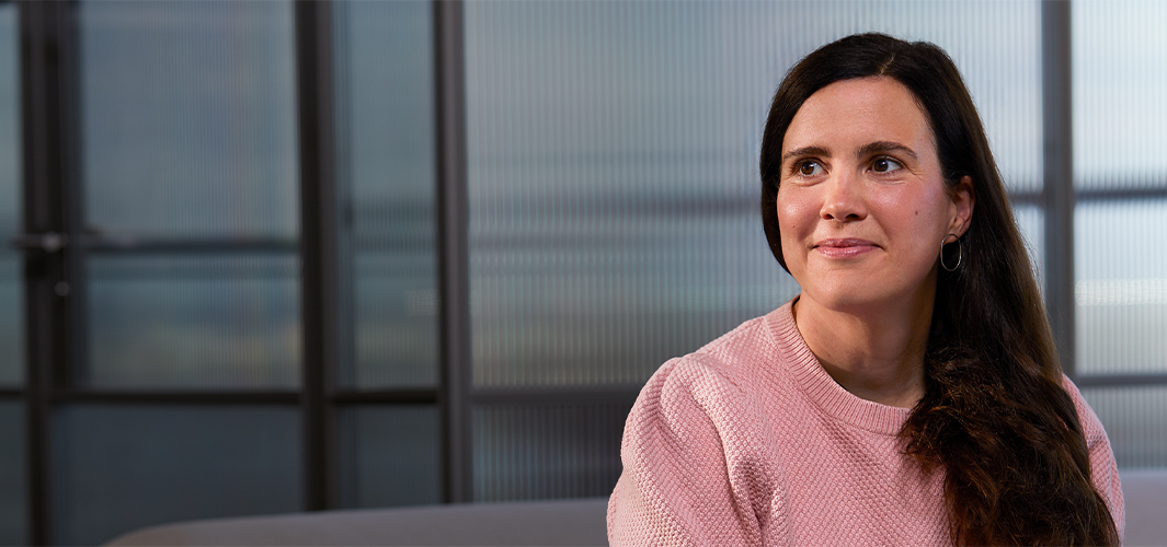 لوسي تجلس في الداخل وخلفها جدار زجاجي شفاف، تبتسم وتنظر إلى الجانب الأيمن.