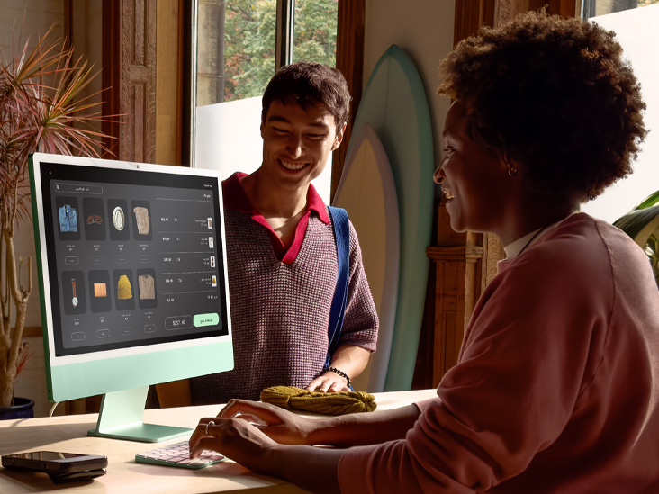 شخصان في غرفة مضاءة جيداً، أحدهما يتحقق من طلب على iMac أخضر بشريحة M4‏.