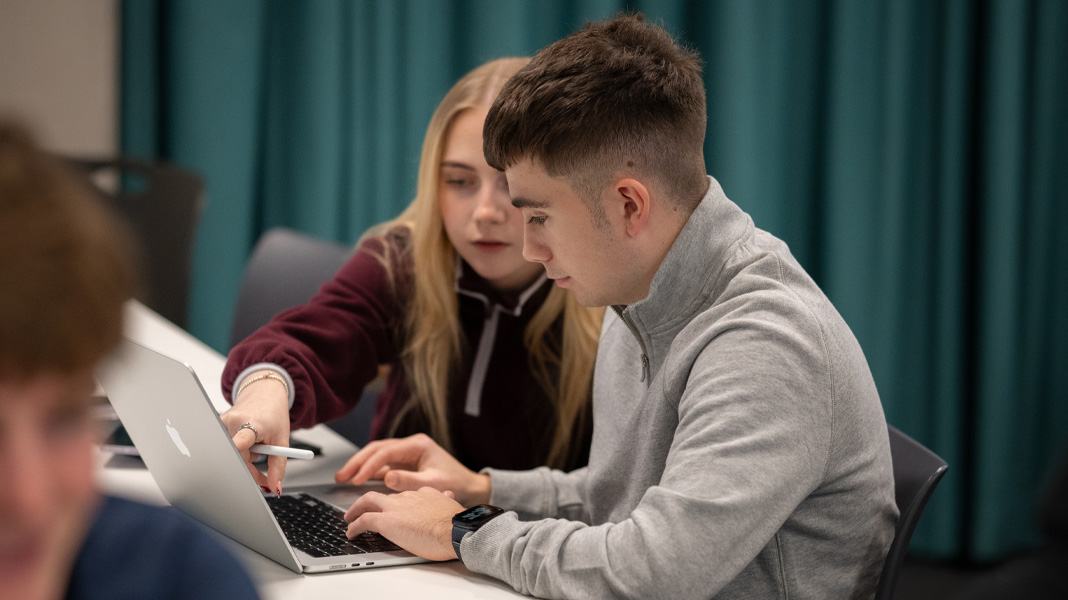 Classmates collaborate on a MacBook, she points at the screen while he types