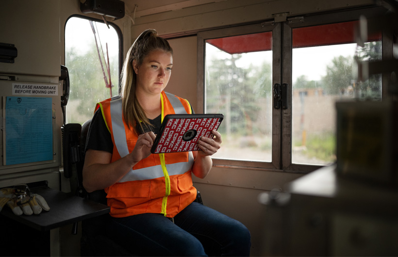 A railroad worker sits inside a stationary train car and references an iPad