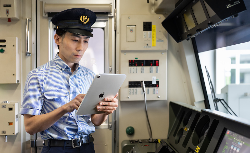A train driver interacts with an iPad while standing in the bright cab of the train he operates.