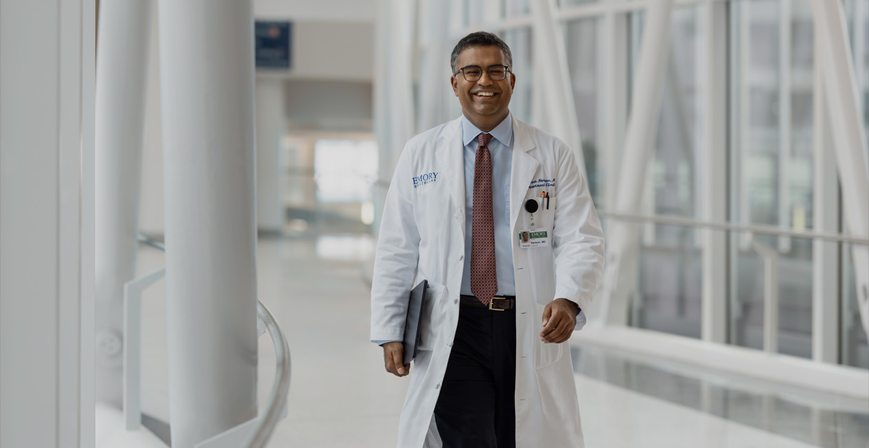 Một bác sĩ đang đi bộ và cầm MacBook dưới cánh tay phải.